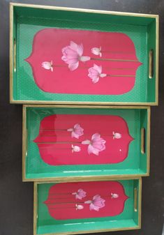 two green trays with pink flowers on them sitting next to each other in front of a black wall