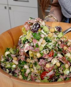 a salad in a wooden bowl with a spoon sticking out of the salad into it