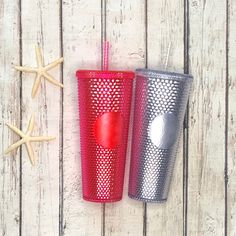 two red and silver cups sitting next to each other on a wooden table with starfish