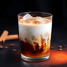 a glass filled with liquid sitting on top of a table next to some coffee beans