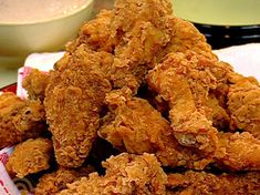 fried chicken is piled on top of a napkin next to a bowl of dipping sauce