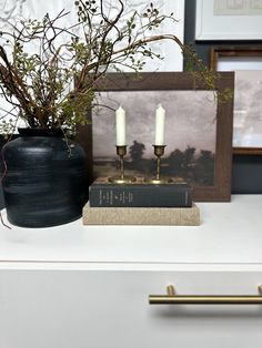 a black vase with two white candles on top of it next to an old book