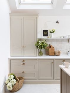 a kitchen with white walls and beige cupboards on the counter top, along with a basket full of flowers