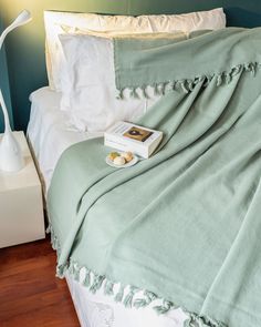 a bed with a green blanket and white pillows on it, next to a lamp