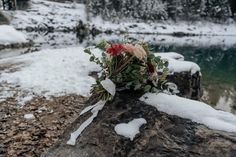 a bouquet of flowers sitting on top of a snow covered rock next to a body of water