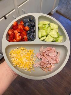 a person holding a plate with different types of food on it, including strawberries, cucumbers and ham