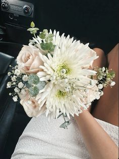 a bridal holding a bouquet of white flowers in her hand while sitting in the back seat of a car