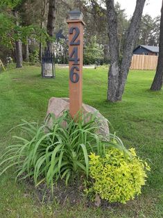 a wooden sign sitting in the middle of a lush green field next to a tree