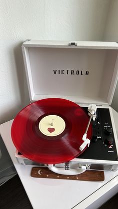 an old record player sitting on top of a white table next to a red vinyl record