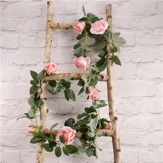 an old ladder is decorated with pink roses and greenery on the outside, against a white brick wall