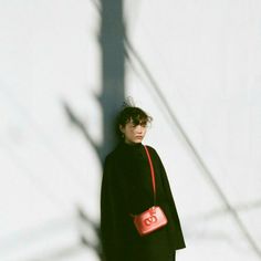 a woman standing in front of a white wall with a red purse on her shoulder