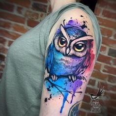 an owl tattoo on the arm with watercolor paint splatters and splashes