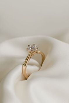 a gold ring with two diamonds sitting on top of white fabric, in the middle of an image