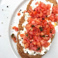 an open face sandwich with tomatoes and cottage cheese on it, sitting on a white plate