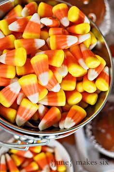 candy corn in a metal bowl on top of a table with other desserts behind it