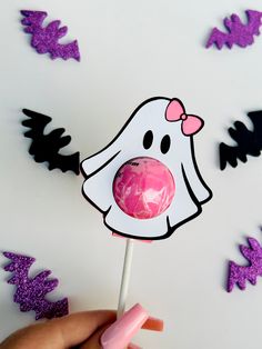 a hand holding a pink lollipop with a ghost on it's stick