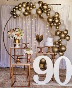 a table topped with gold and white balloons next to a sign that says 90th