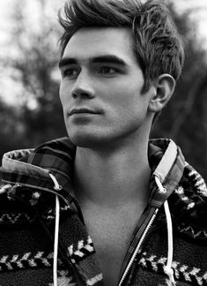 a young man is wearing a jacket and posing for a black and white photo with trees in the background