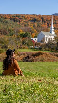 a woman sitting on top of a lush green field next to a white church in the background