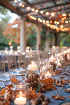 candles are lit on the table with leaves and acorns around it in front of an outdoor gazebo