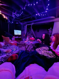 two women sitting on couches in a room with purple lights hanging from the ceiling