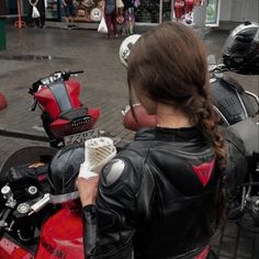 a woman in black leather jacket standing next to red and white motorcycle parked on street