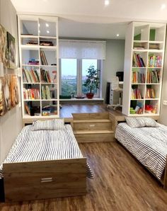 two beds in a room with bookshelves on the wall and wooden flooring