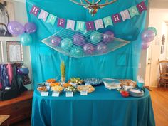 a birthday party with balloons, cake and snacks on a table in front of a blue backdrop