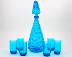 a blue glass vase with six glasses in front of it