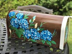 a brown leather purse with blue flowers painted on the front and sides, sitting on a metal bench