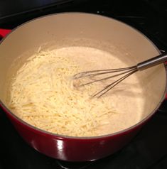 a red pan filled with cheese and whisk on top of a gas stove