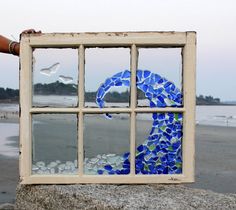 a hand holding a window pane with a blue and green mosaic design on it