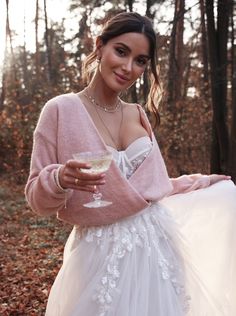 a woman in a white dress and pink sweater holding a wine glass with her right hand