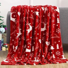 a red christmas blanket with white deers and snowflakes on it in front of a couch