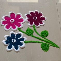 three different colored flowers on a white surface