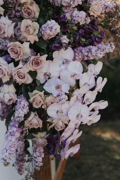 purple and white flowers are arranged in a vase on a table outside with greenery