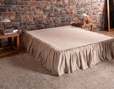 a bed with a tan ruffled bedskirt in front of a brick wall