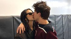 a man and woman kissing each other in front of a black leather couch with white walls