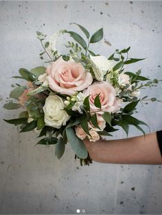 a person holding a bouquet of white and pink flowers with greenery in their hand