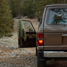 the back end of a brown truck parked on top of a rocky road next to trees