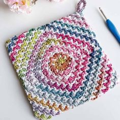 a crocheted pot holder next to some flowers and a pair of blue scissors