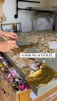 a woman is painting with gold foil on a table in front of a white background that says, a little bit of gold