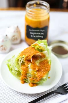 a white plate topped with lettuce covered in sauce next to a jar of mustard