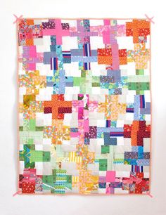 a colorful quilt hanging on the wall in front of a white wall with pink trim