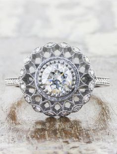 an old - fashioned diamond ring is displayed on a marble surface, with the center surrounded by filigrees