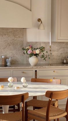 a kitchen table with four chairs and a vase filled with flowers on top of it