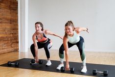 two women doing push ups with dumbbells on a mat in an empty room