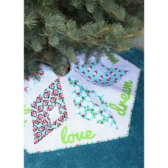 the tree is next to two quilted placemats on the floor near a pine tree