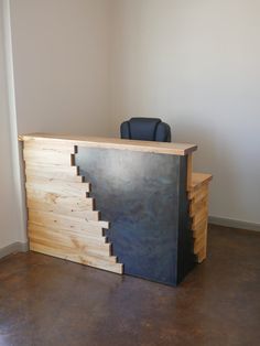 a wooden desk with a black chair sitting on it's side in front of a white wall