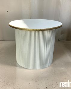 a round white table with gold trim around the top and bottom, sitting on a concrete floor